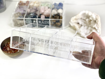 An empty acrylic box in hand with crsyatls in the background.