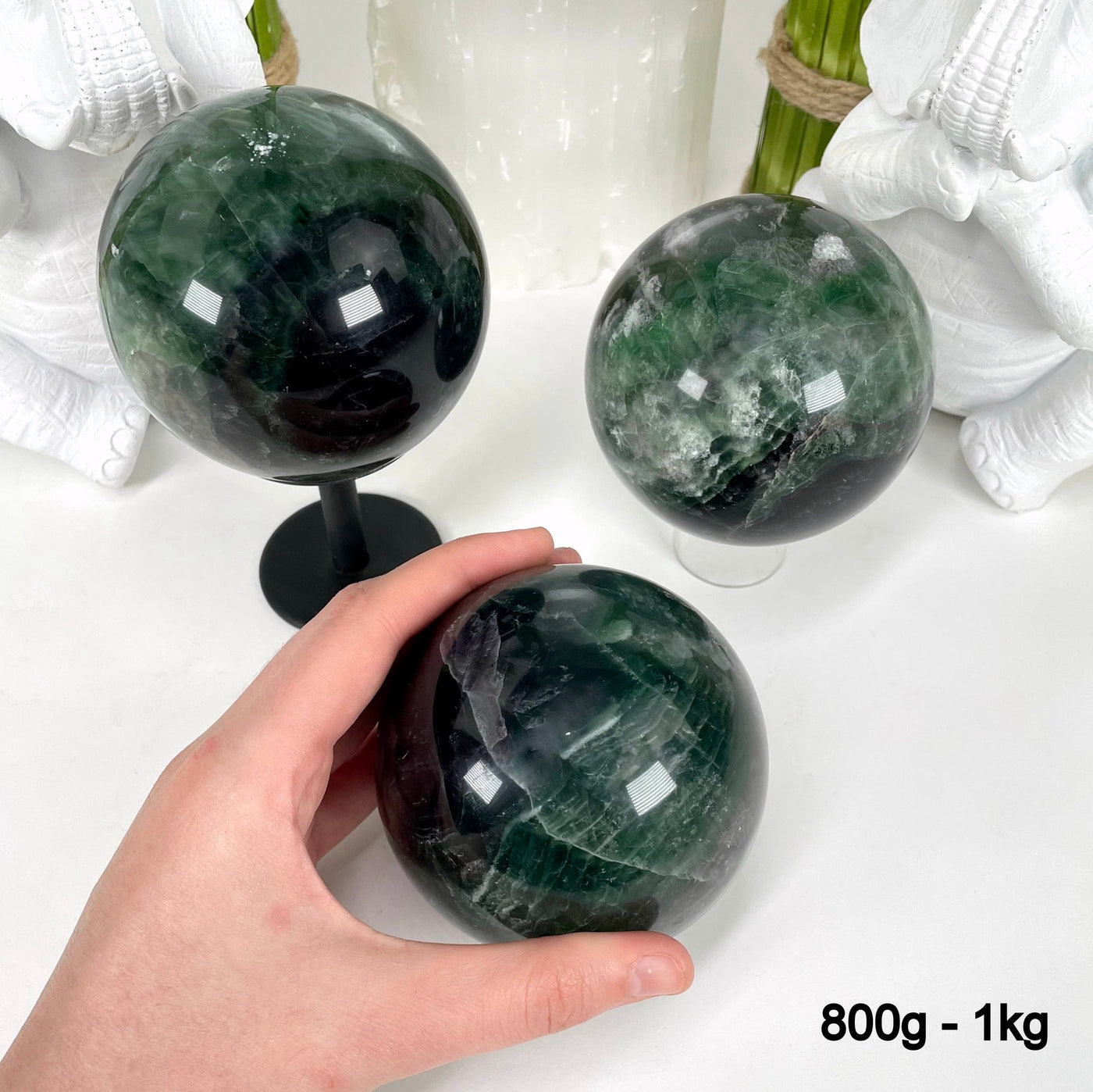 three 800g - 1kg rainbow fluorite polished spheres on display in front of backdrop for possible variations with one in hand for size reference