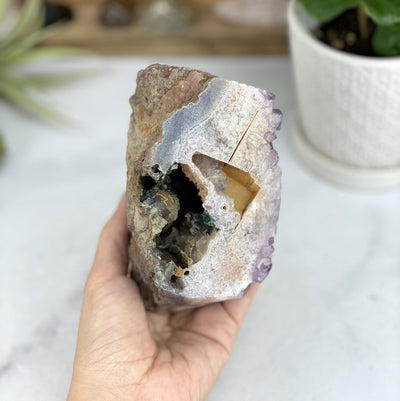 hand holding up Amethyst Crystal Cut Base Stone with decorations in the background