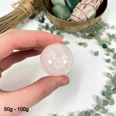 one 50g - 100g rose quartz polished sphere in hand for size reference