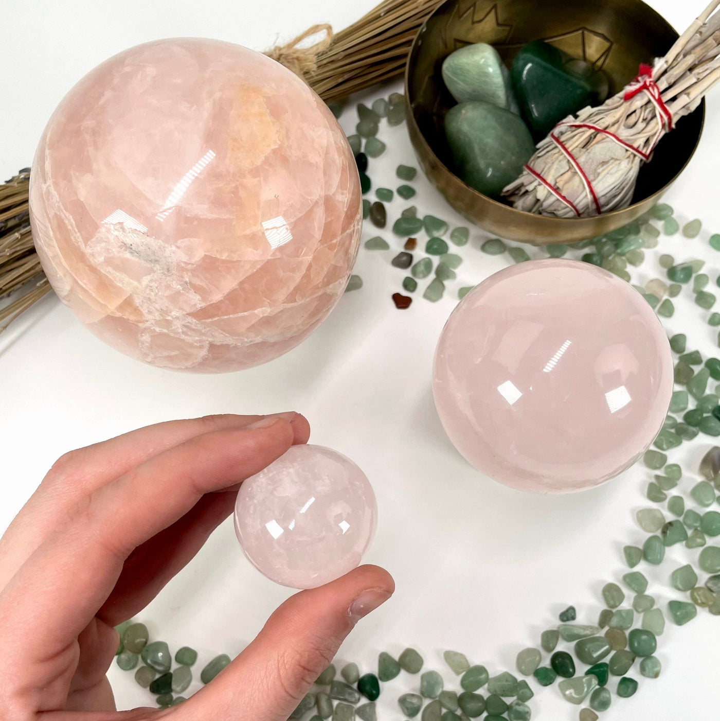three different rose quartz polished sphere weights on display for size comparison with one in hand 