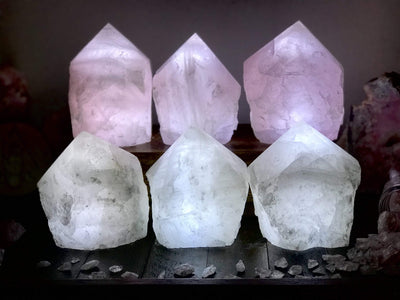 6 Rose Quartz and Crystal Lamps lit up in a dark room with other crystals as decoration