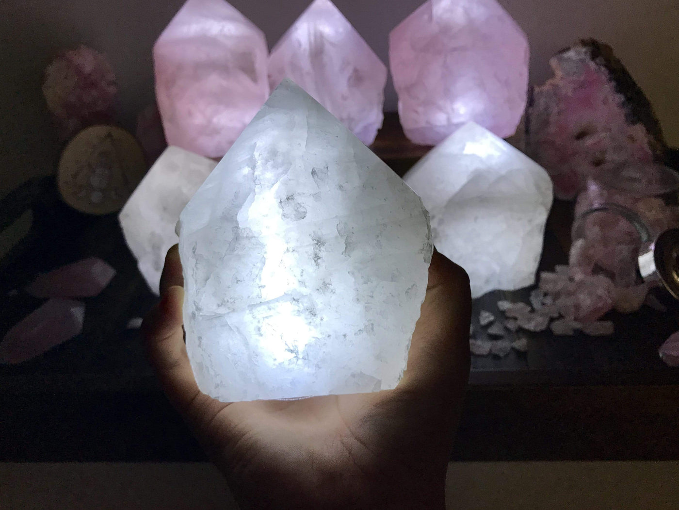 Hand holding up Crystal Quartz Lamp with other lamps lit up with other crystals in the background