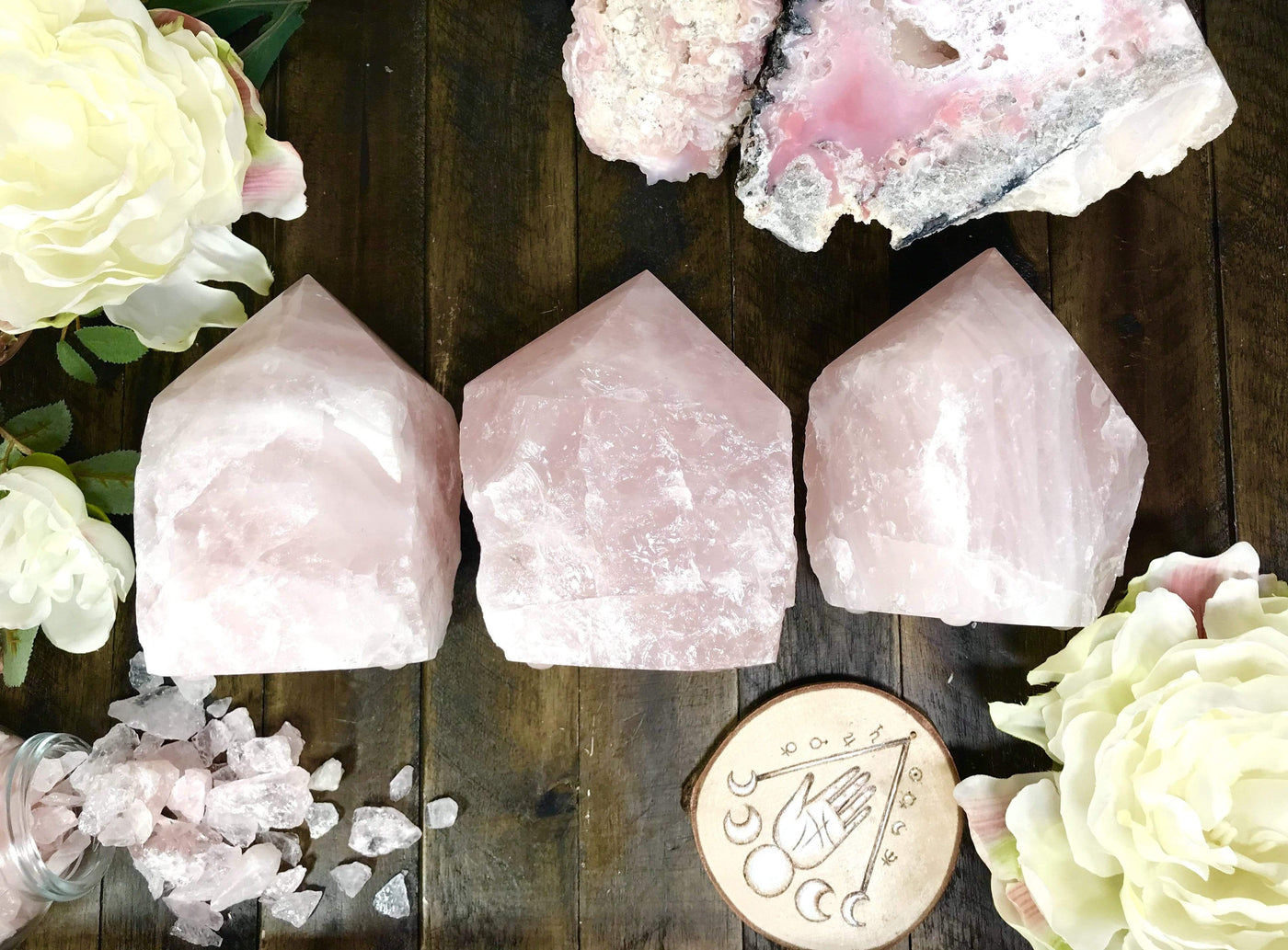 3 rose Quartz lamps lined up with other crystals and flowers on wooden table