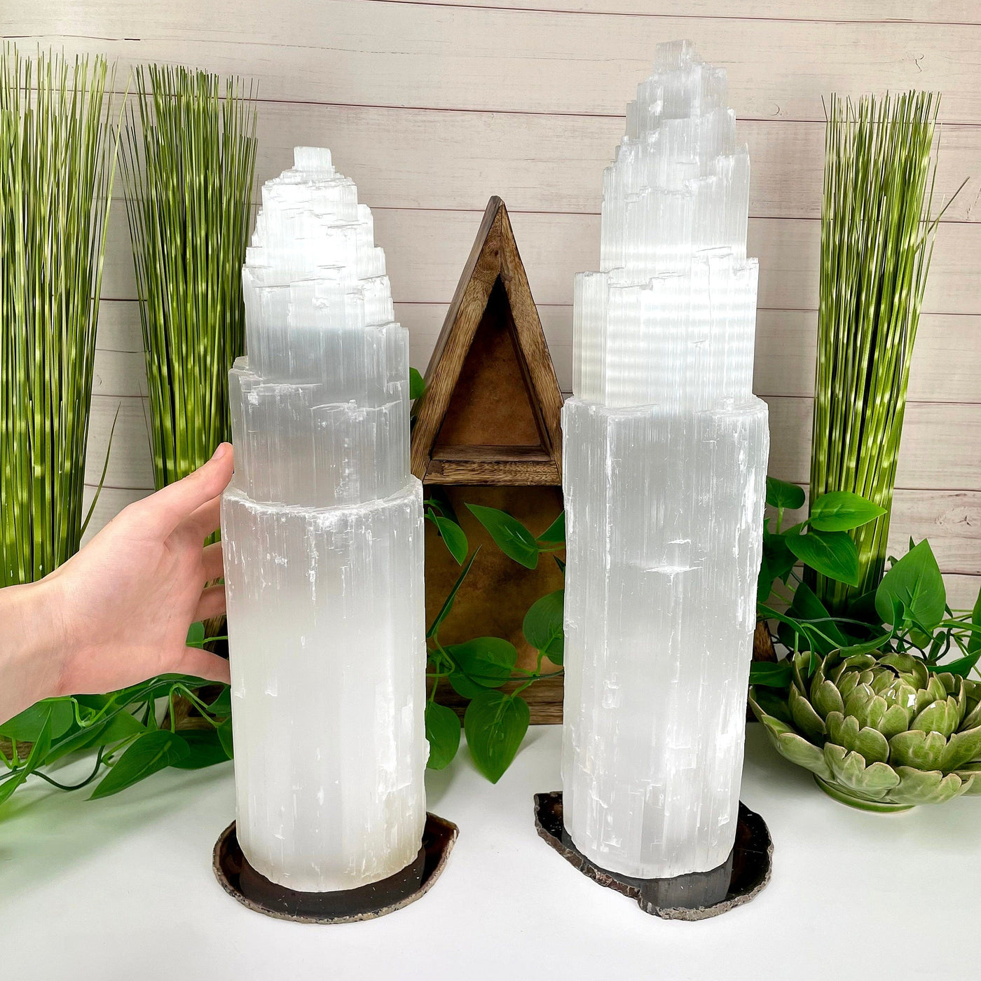 two selenite xxl lamps on display in front of backdrop for possible variations with a hand on one of them for size reference
