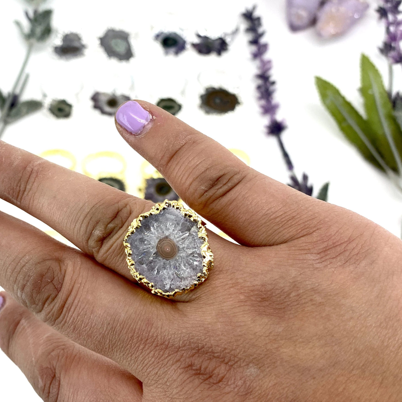 hand wearing gold amethyst stalactite ring with decorations blurred in the background