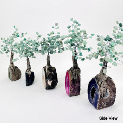 side view of multiple colored geode trees with green quartz tumbled stones on the top portion displaying the different thicknesses 