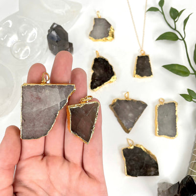 two smokey quartz slab pendants in hand for possible sizes and variations with many others in background display