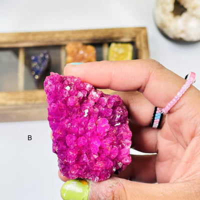 Hand holding up close of the (B) vibrant Pink Dyed Amethyst Cluster on white background