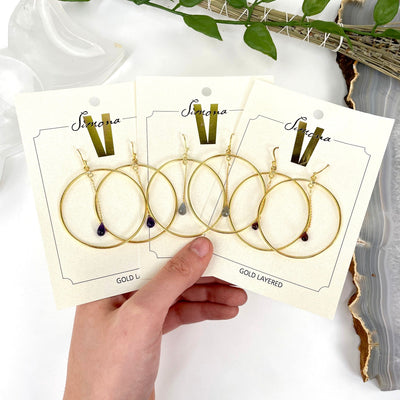 three sets of gemstone hoop earrings on packaging display in hand 