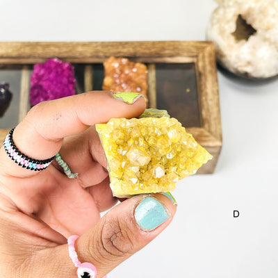 Hand holding up the vibrant (D) Yellow Dyed Amethyst Cluster on white background