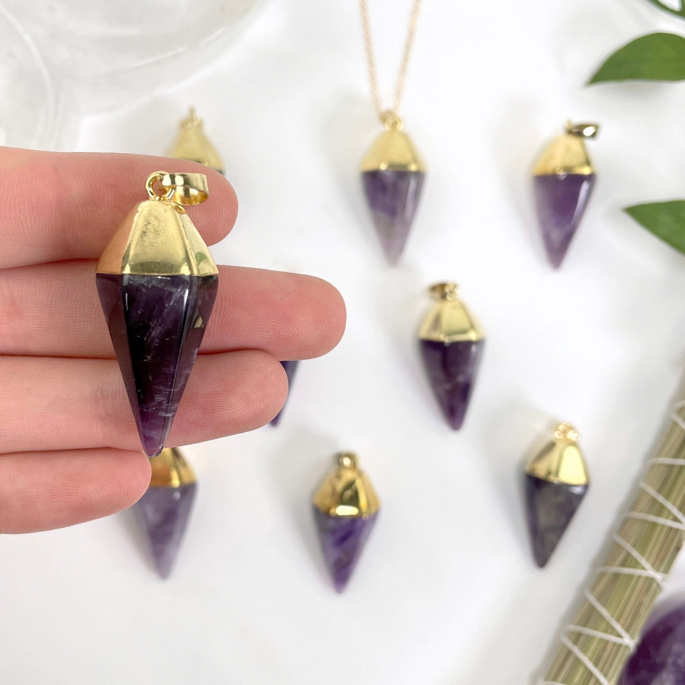 close up of one amethyst quartz spear pendant in hand for size reference and details with many others in the background
