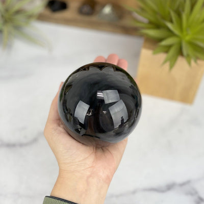 hand holding up Black Obsidian Sphere with decorations in the background