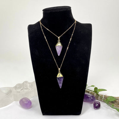 two amethyst quartz spear pendants on a chain at two different lengths on a bust display