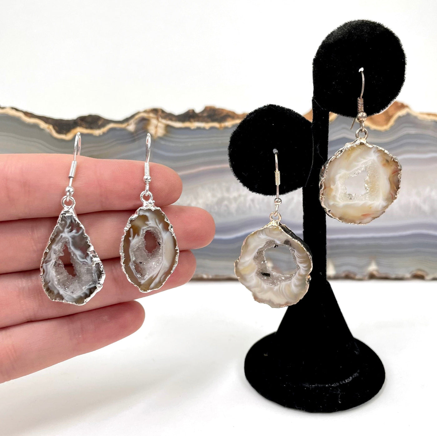 one pair of agate druzy slice earrings in hand for size reference with another pair on earring display