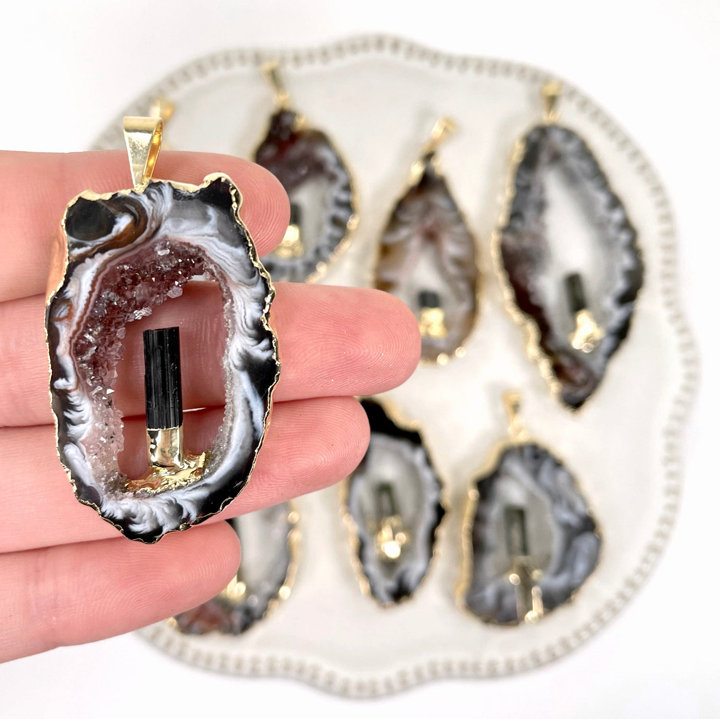 close up of one agate druzy slice pendant in hand for size reference and details with many others in the background
