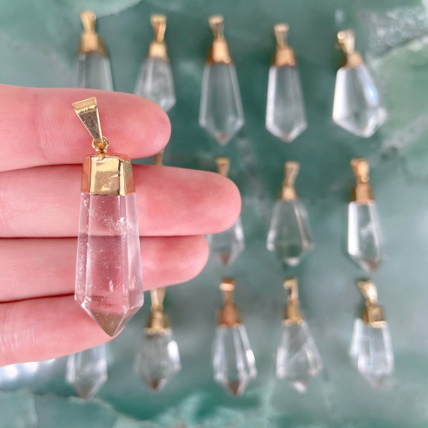close up of one fancy crystal quartz point pendant in hand for size reference and details with many others in the background