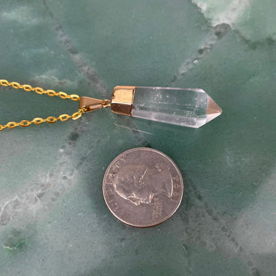 angled view of one fancy crystal quartz point pendant on a chain with a quarter for size reference