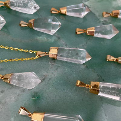 angled view of many fancy crystal quartz point pendants laying flat with one of them on a chain