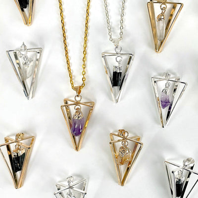 many dangle stone point pendulum pendants on white background with one gold and one silver one on chains