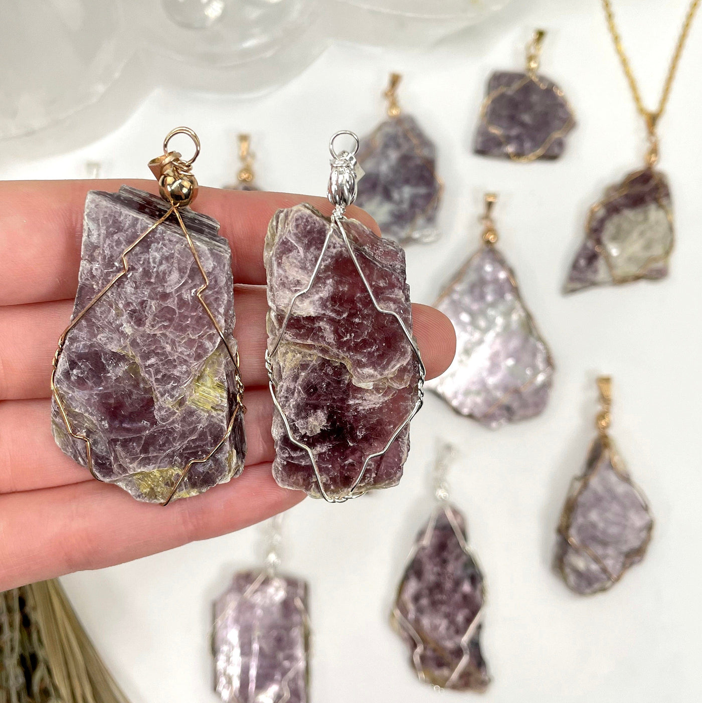 close up of one gold and one silver purple mica wire wrapped pendants in hand for size reference and possible variations with many others in the background