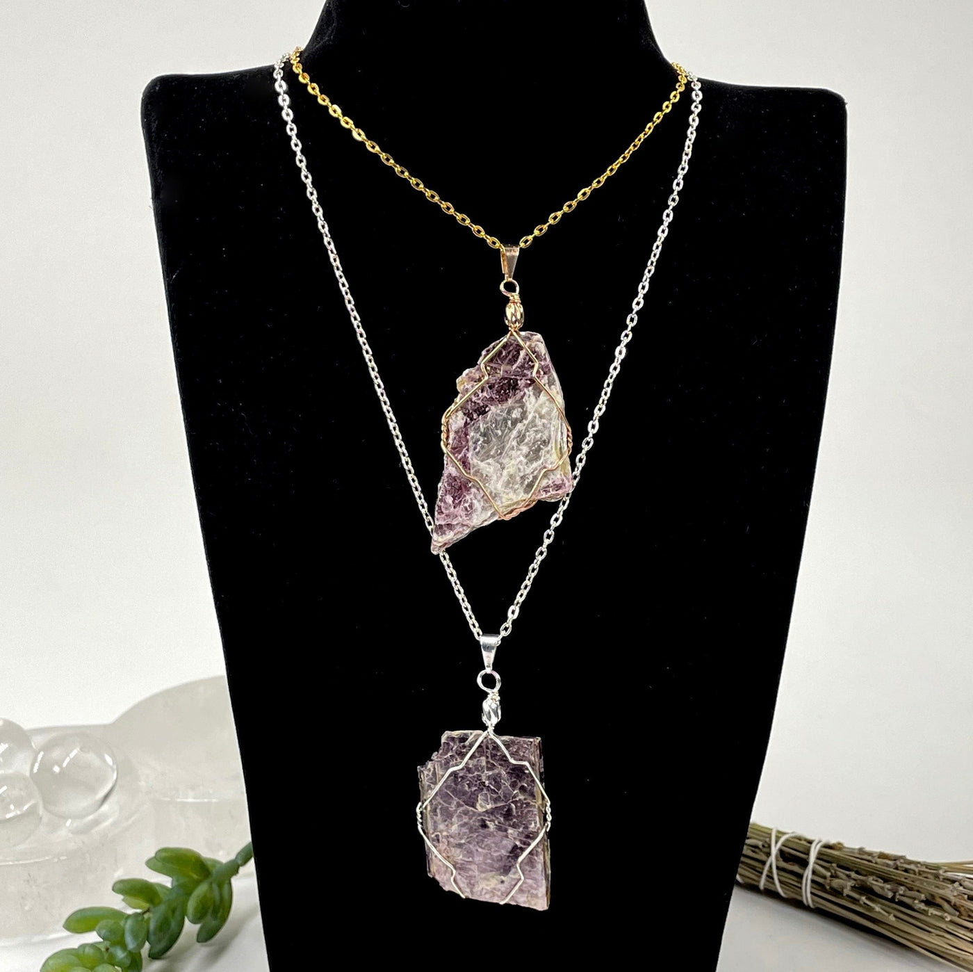 one gold and one silver purple mica wire wrapped pendants hanging on chains on bust display