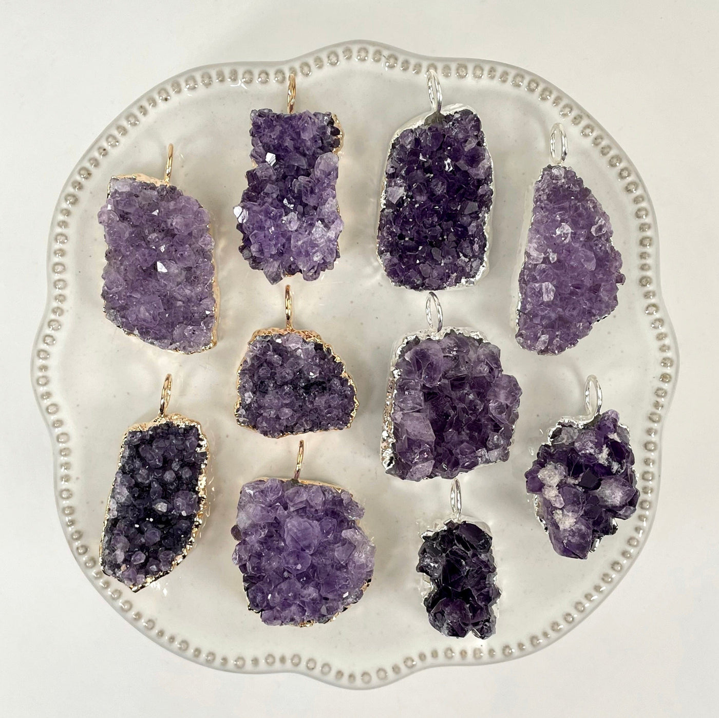 overhead view of many gold and silver freeform amethyst druzy cluster pendants on display on white background for possible variations