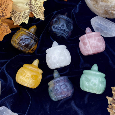 7 different Carved Pumpkin Jack-o'-lantern Gemstones displayed on a velvet surface.