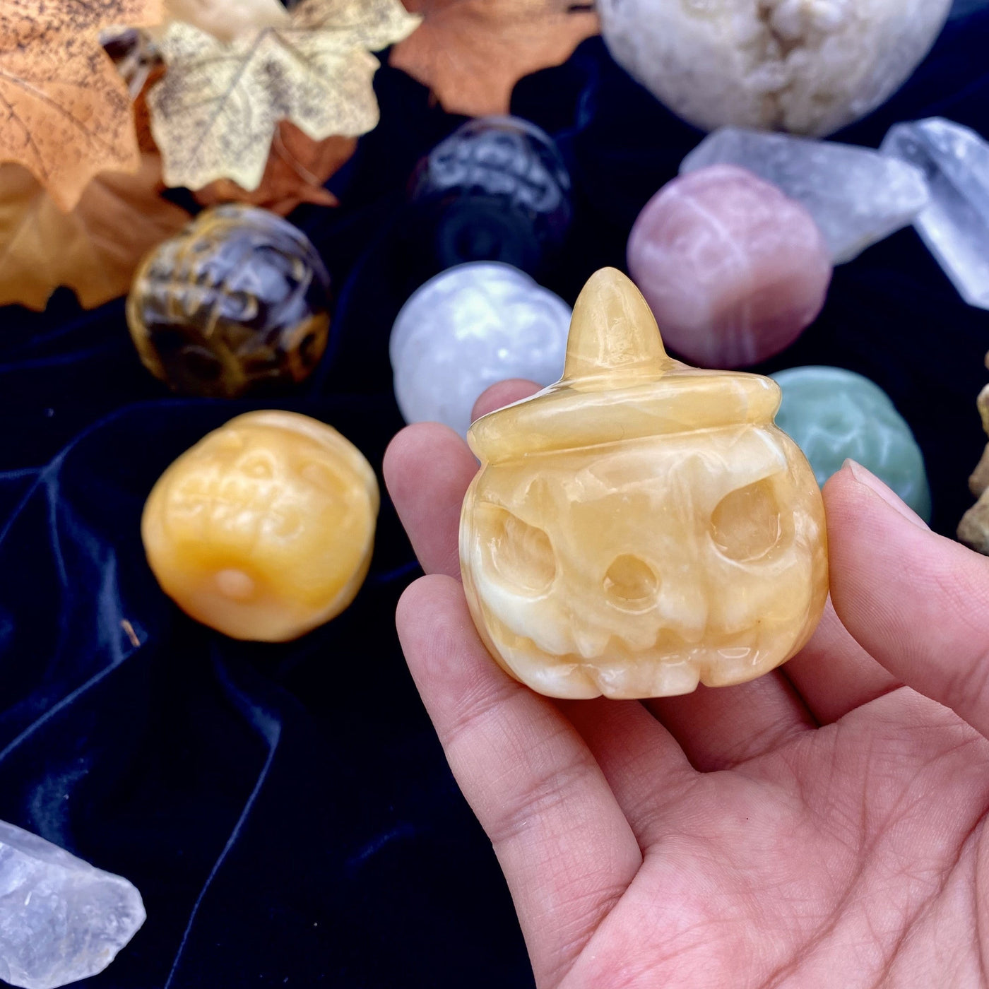Frontal view of a Orange Citrine Carved Pumpkin Jack-o'-lantern Gemstone held in a woman's hand.