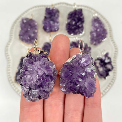 close up of one gold and one silver freeform amethyst druzy cluster pendant for possible variations and details with many others on display in the background