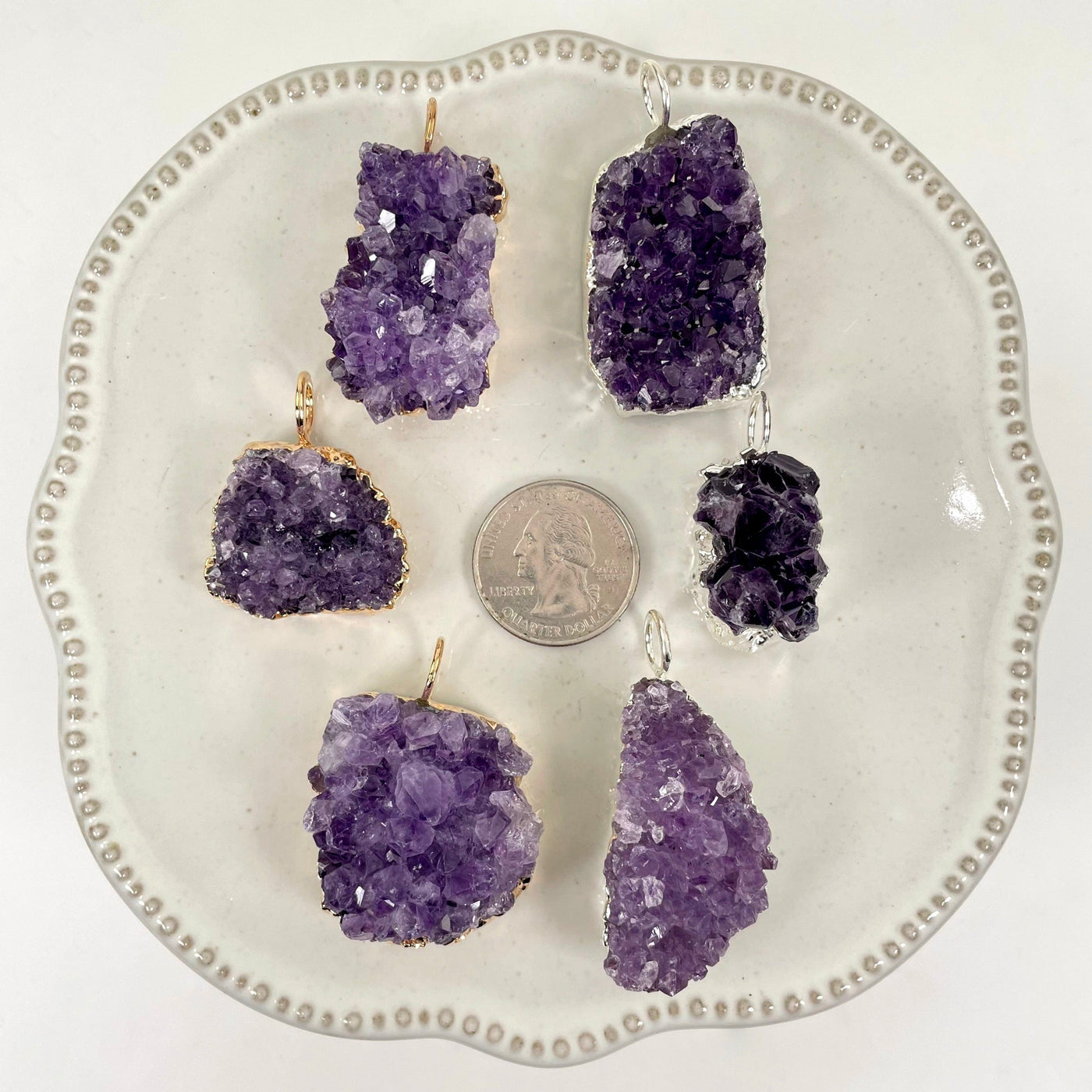 overhead view of three gold and three silver freeform amethyst druzy cluster pendants on display on white background with a quarter for size reference