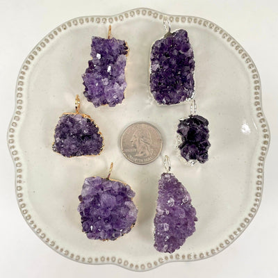 overhead view of three gold and three silver freeform amethyst druzy cluster pendants on display on white background with a quarter for size reference
