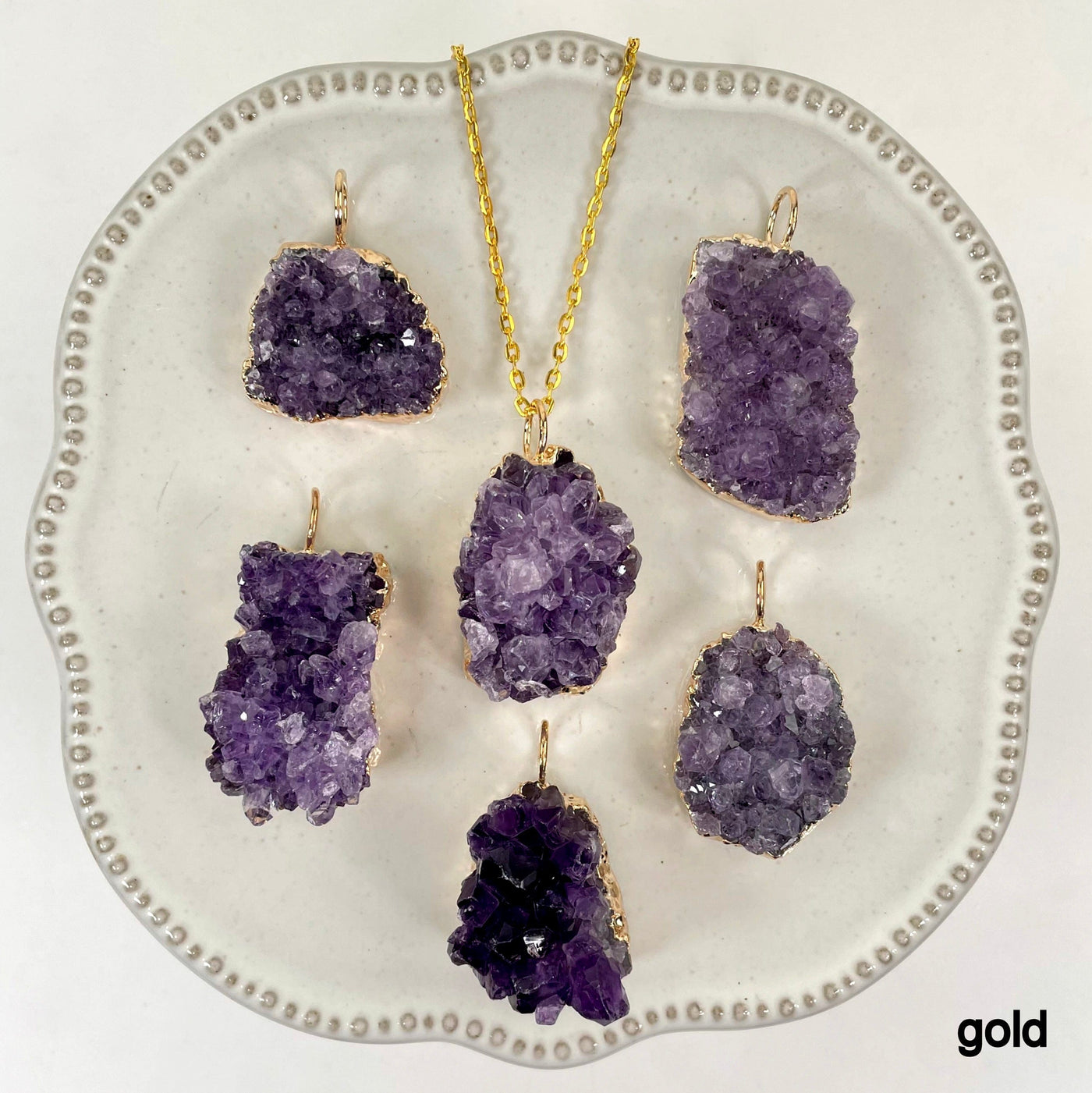many gold freeform amethyst druzy cluster pendants on display on white background with one of them on a gold chain