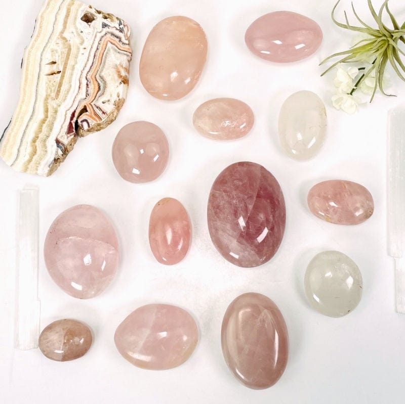 multiple rose quartz palm stones showing different sizes and colors patterns on a white background 