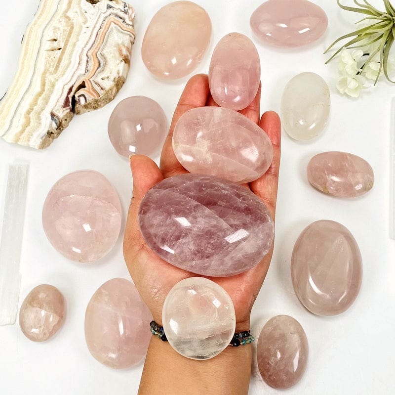 multiple rose quartz palm stones in hand showing different sizes and colors patterns 