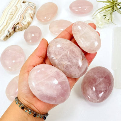 multiple rose quartz palm stones in hand showing different possible sizes 