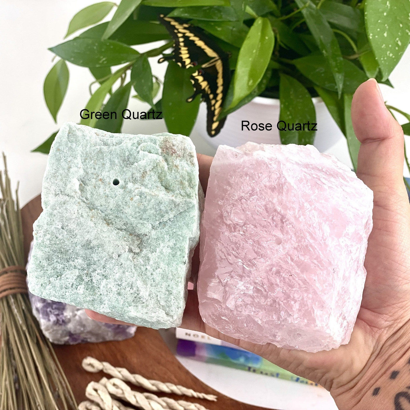 Hand holding 1 green quartz Rough Stone Incense Burner and 1 rose quartz Rough Stone Incense Burner with decorations in the background