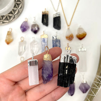 close up of three different gemstone point pendant options in hand for possible variations with many others in the background