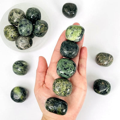 nephrite tumbled stones in hand showing the different possible color shades and patterns 