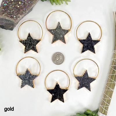 overhead view of six gold druzy star pendants on white background with a quarter for size reference