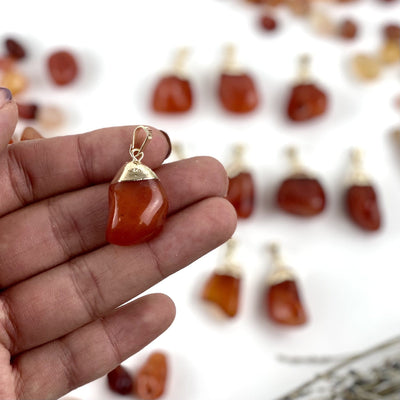 hand holding up Tumbled Carnelian Pendant with Electroplated 24k Gold Cap with others blurred in the background
