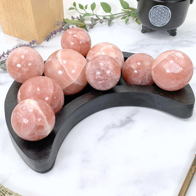 A MULTITUDE OF ROSE CALCITE SPHERES IN A BLACK MOON BOWL WITH A MARBLE BACKGROUND