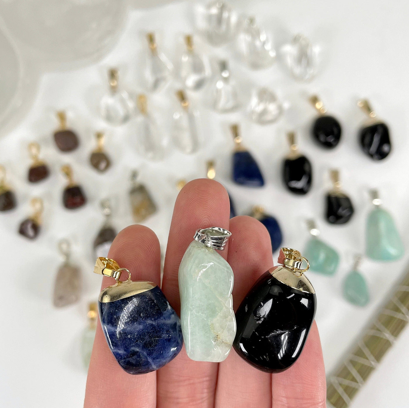 close up of three different tumbled gemstone pendants for possible options and size reference with many others in the background