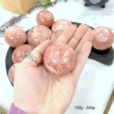 100gram - 200gram rose calcite sphere in hand with marble background