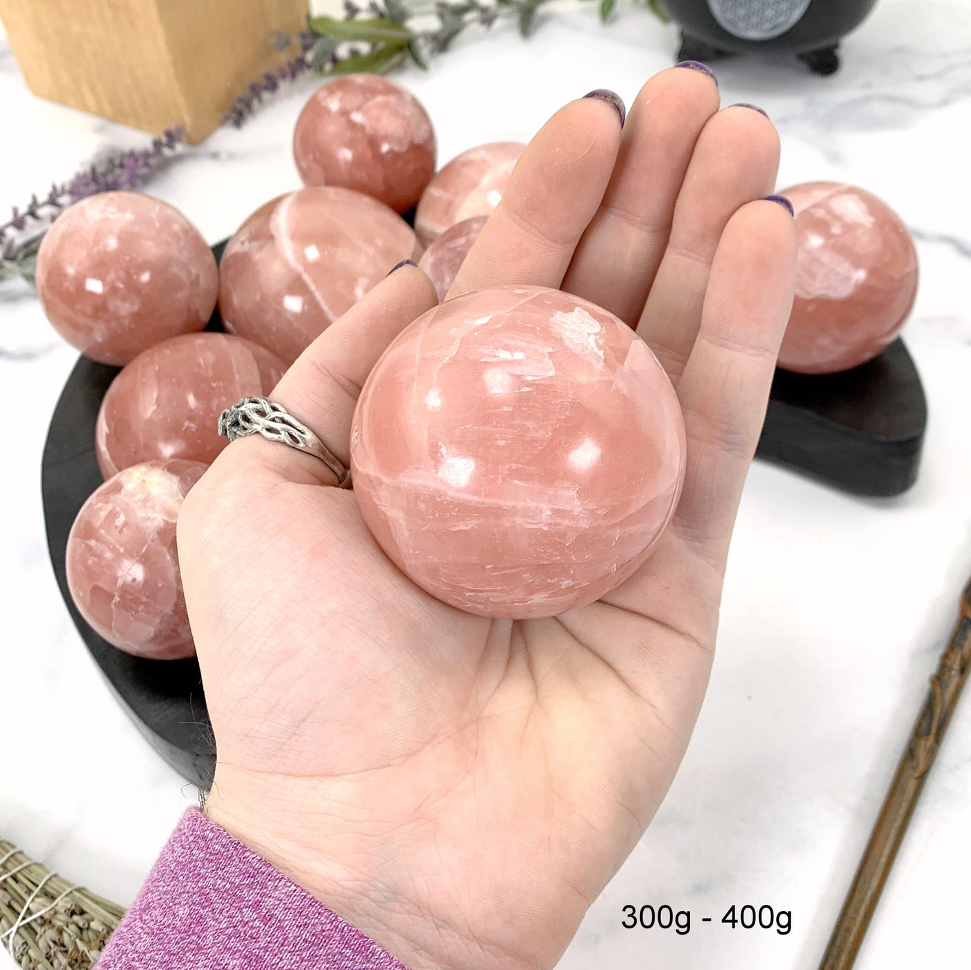 300gram - 400gram rose calcite sphere in hand with marble background