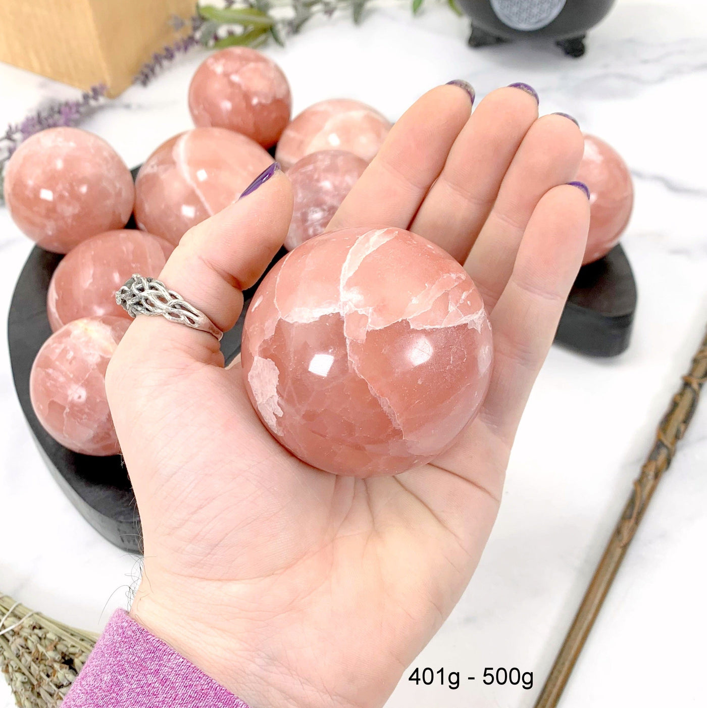 401gram - 500gram rose calcite sphere in hand with marble background