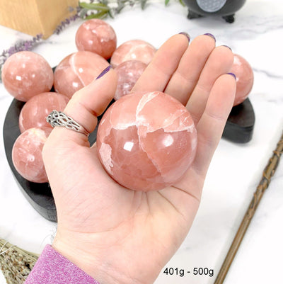401gram - 500gram rose calcite sphere in hand with marble background