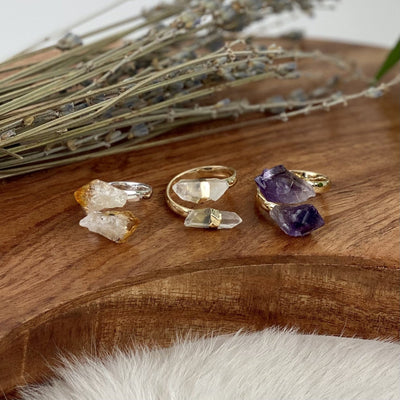 Citrine Double Point Ring in silver, Crystal quartz Double Point Ring in 24k Gold Electroplated, and Amethyst Double Point Ring in 24k Gold Electroplated on a wood base 