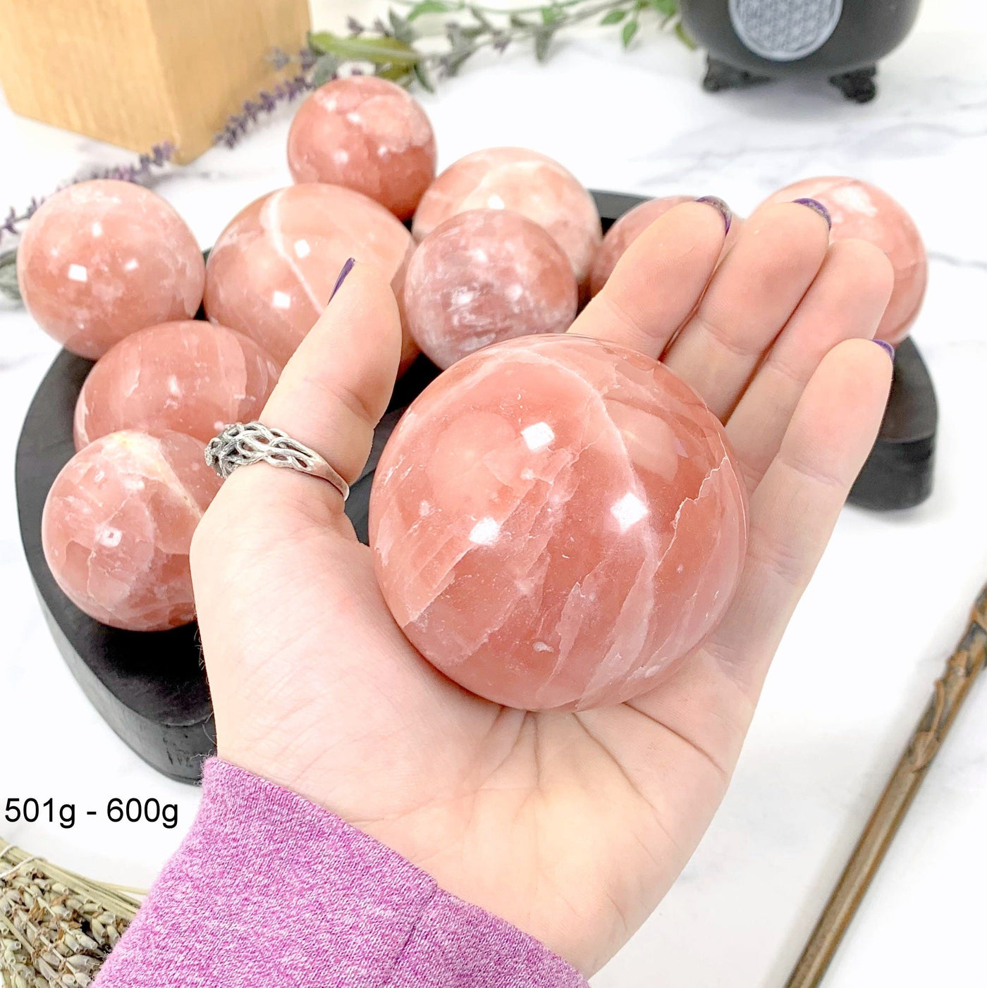 501gram - 600gram rose calcite sphere in hand with marble background