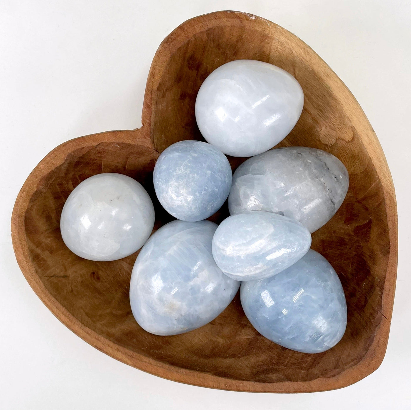 overhead view of many blue calcite polished eggs in a heart bowl